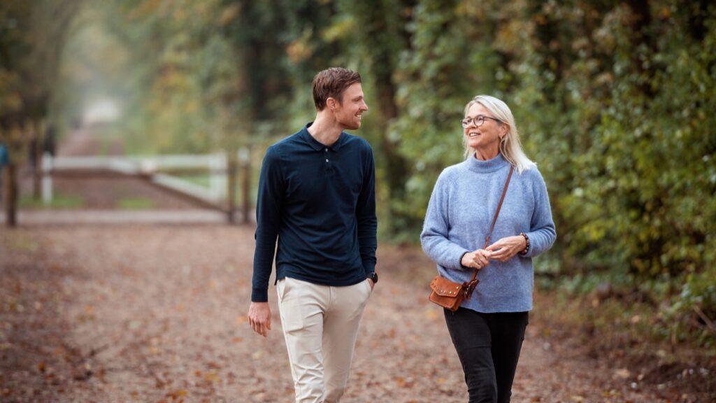 A man and an older woman walking along a tree-lined path