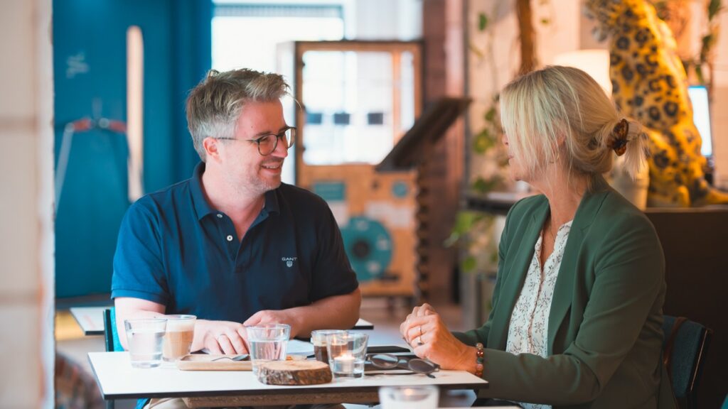A man with glasses and a blonde woman at a cafe table