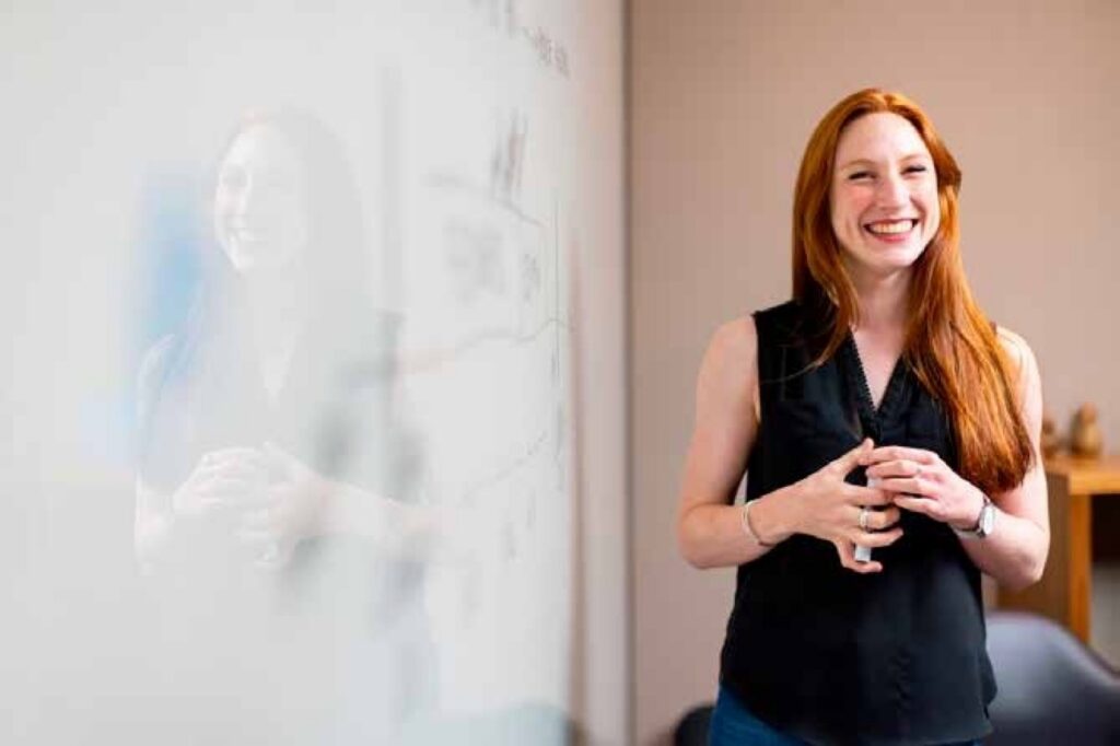 A red-haired woman laughing in front of a whiteboard